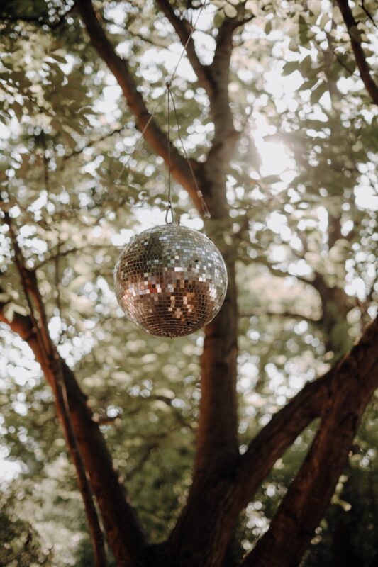 Discokugel als Dekoration im Biergarten, hängt in einem Baum und wird von der Sonne angestrahlt