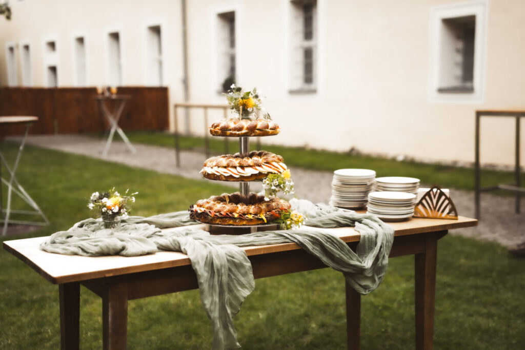 Dreistöckige Hochzeits-Brezen-Torte mit Blumen dekoriert auf einem Holztisch im Innenhof bei strahlendem Sonnenschein.