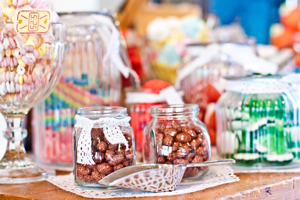 Verschiedene Süßigkeiten in Vintage-Glässchen und Schalen schön dekoriert mit Spitzenbändchen und Deckchen an einer Candybar in der Eventlocation.