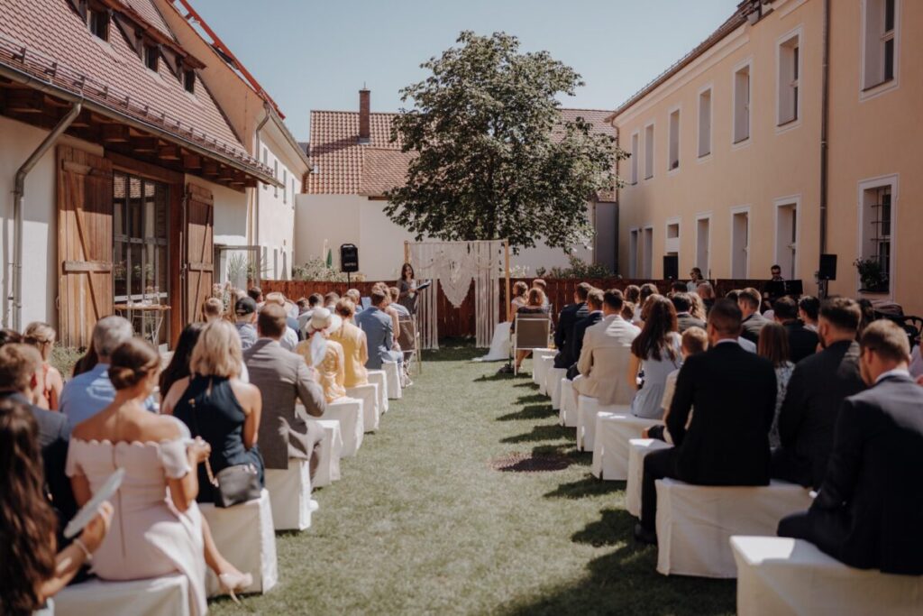 Brautpaar im Innenhof des Spitalstadls während einen freien Trauung, im Hintergrund ein Makramee-Boho-Traubogen.