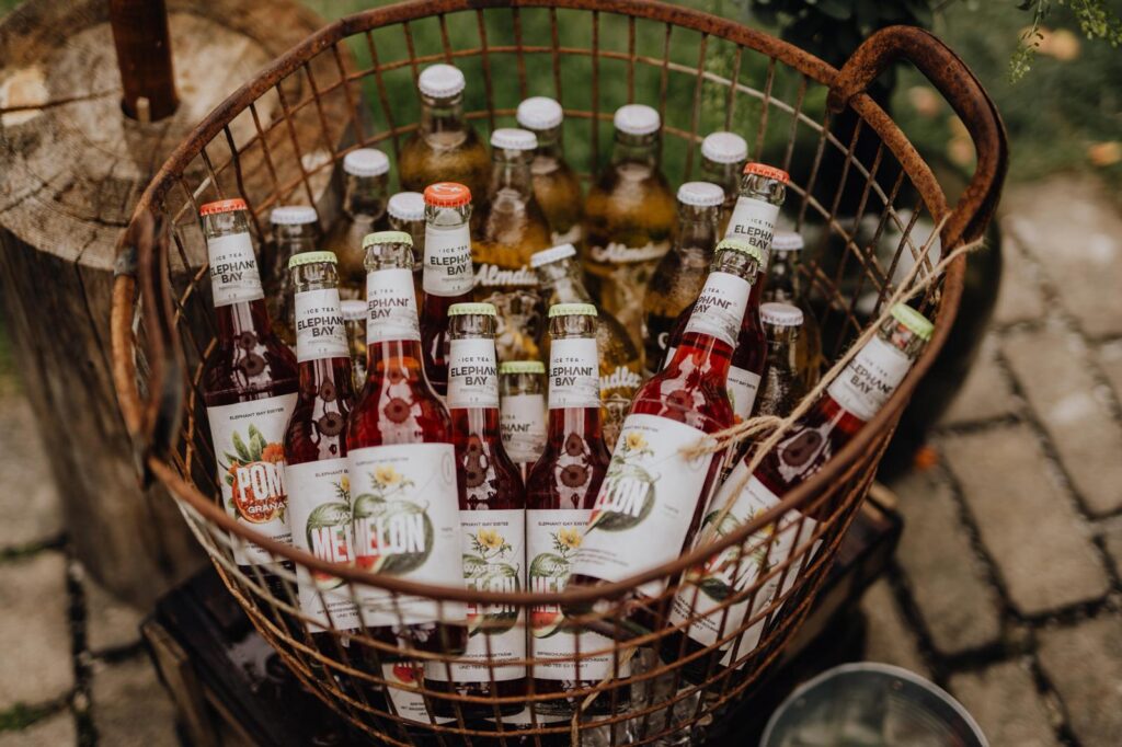 Limonadenkorb mit Aldmdudler und Eistee in Flaschen, Antiker Drahtkorb in dem die Flaschen arrangiert sind, darüber Eiswürfel um die Getränke küühl zu halten.