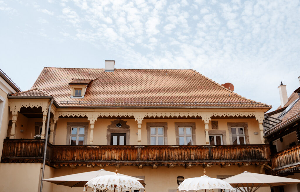 Altes Gebäude mit verziertem Holzbalkon, blauer Himmel im Hintergrund, perfektes Hochzeits-Wetter.
