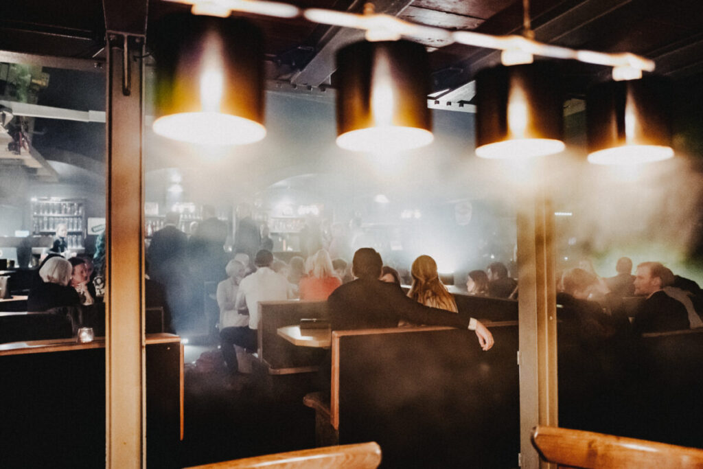 Gäste sitzen in den Sitzgruppen während einer Afterparty, der Raum ist voller Nebel.