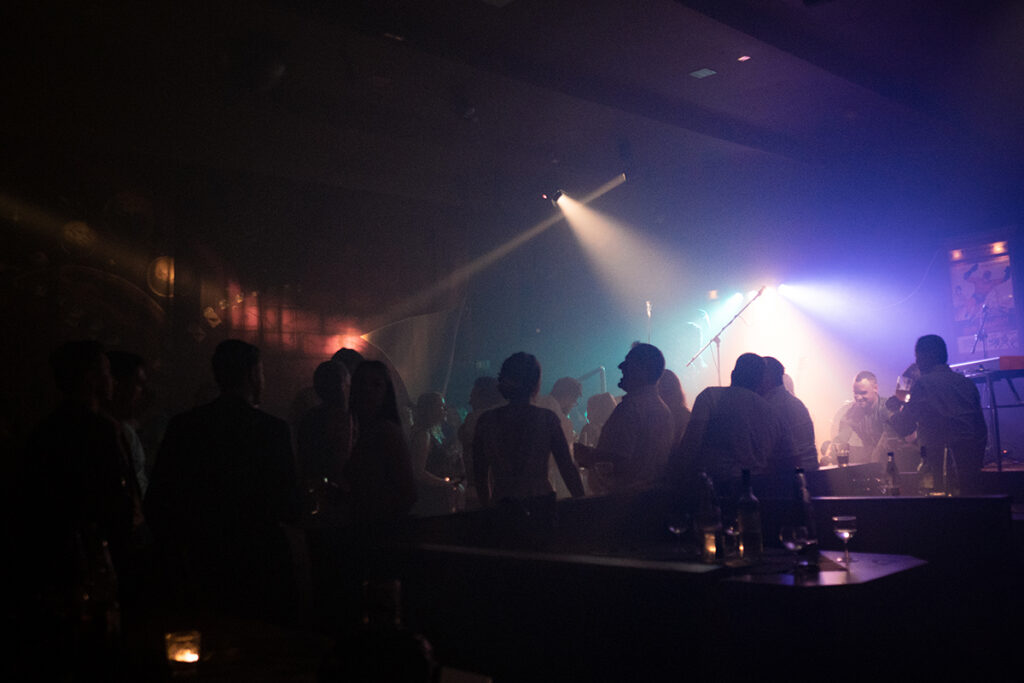 Gäste tanzen auf der Tanzfläche während einer Brautentführung, es sind Lichteffekte zu sehen und lachende Menschen. Auf den Tischen im Vordergrund stehen Getränke.